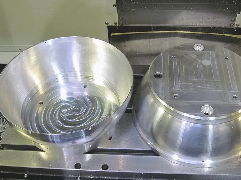 Two large machined aluminum domes on a machine table, one concave and one convex