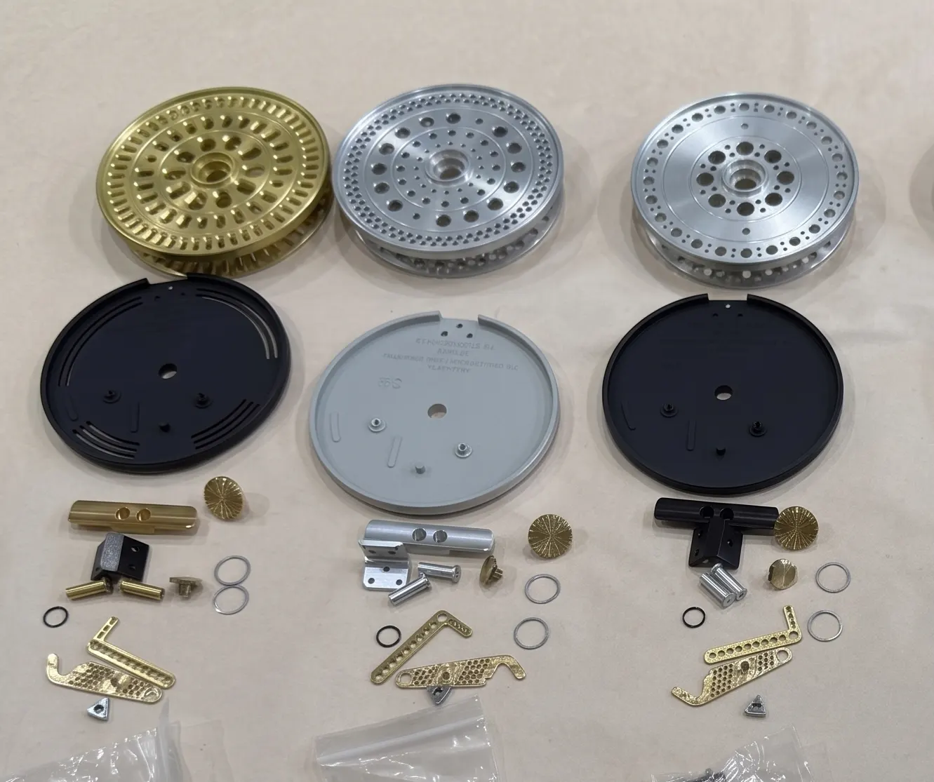 Machined fly reel components — spools, frames, handles, and hardware — laid out before assembly.