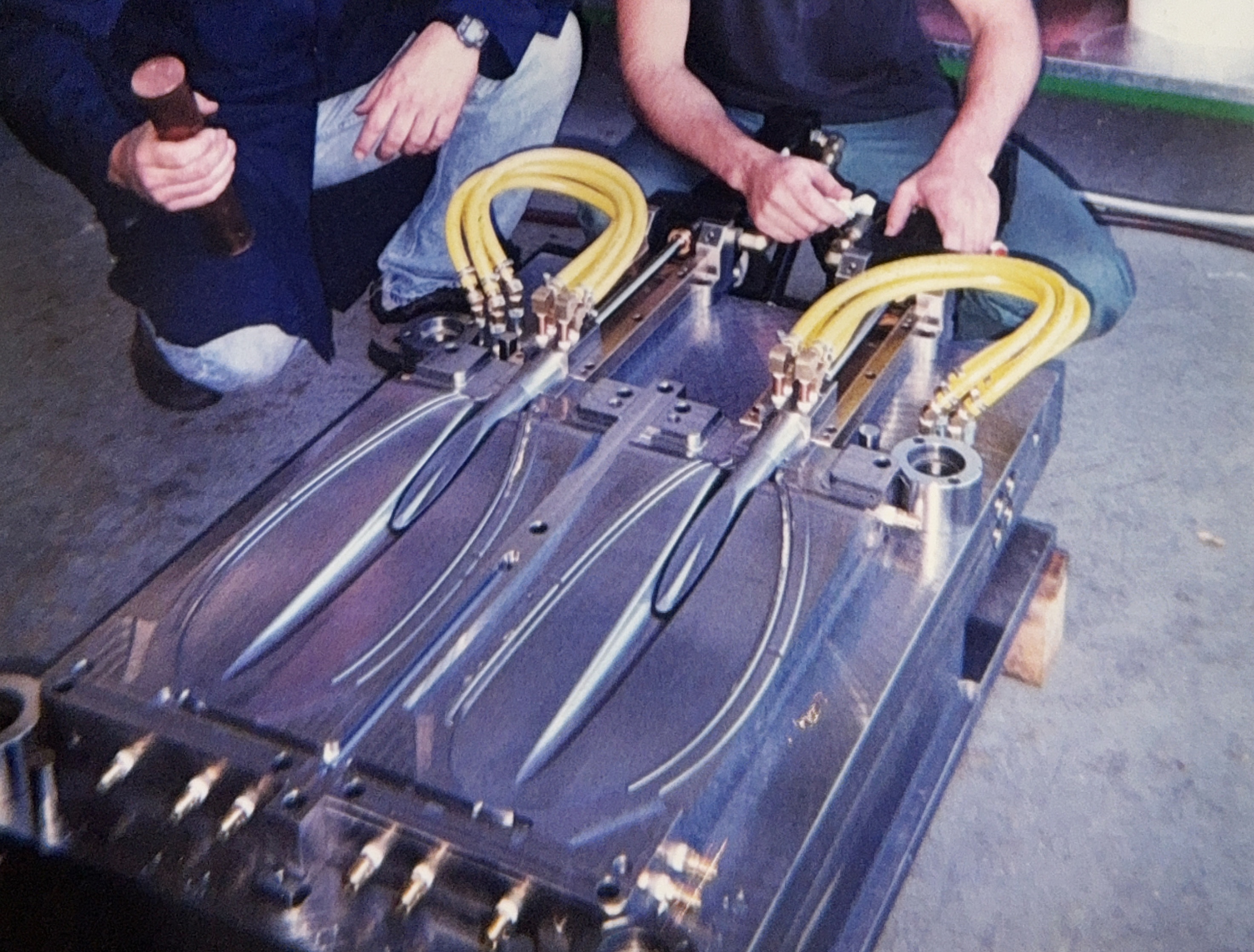 Multi-cavity steel injection mould for kayak paddle blades, connected to hydraulic lines during setup.