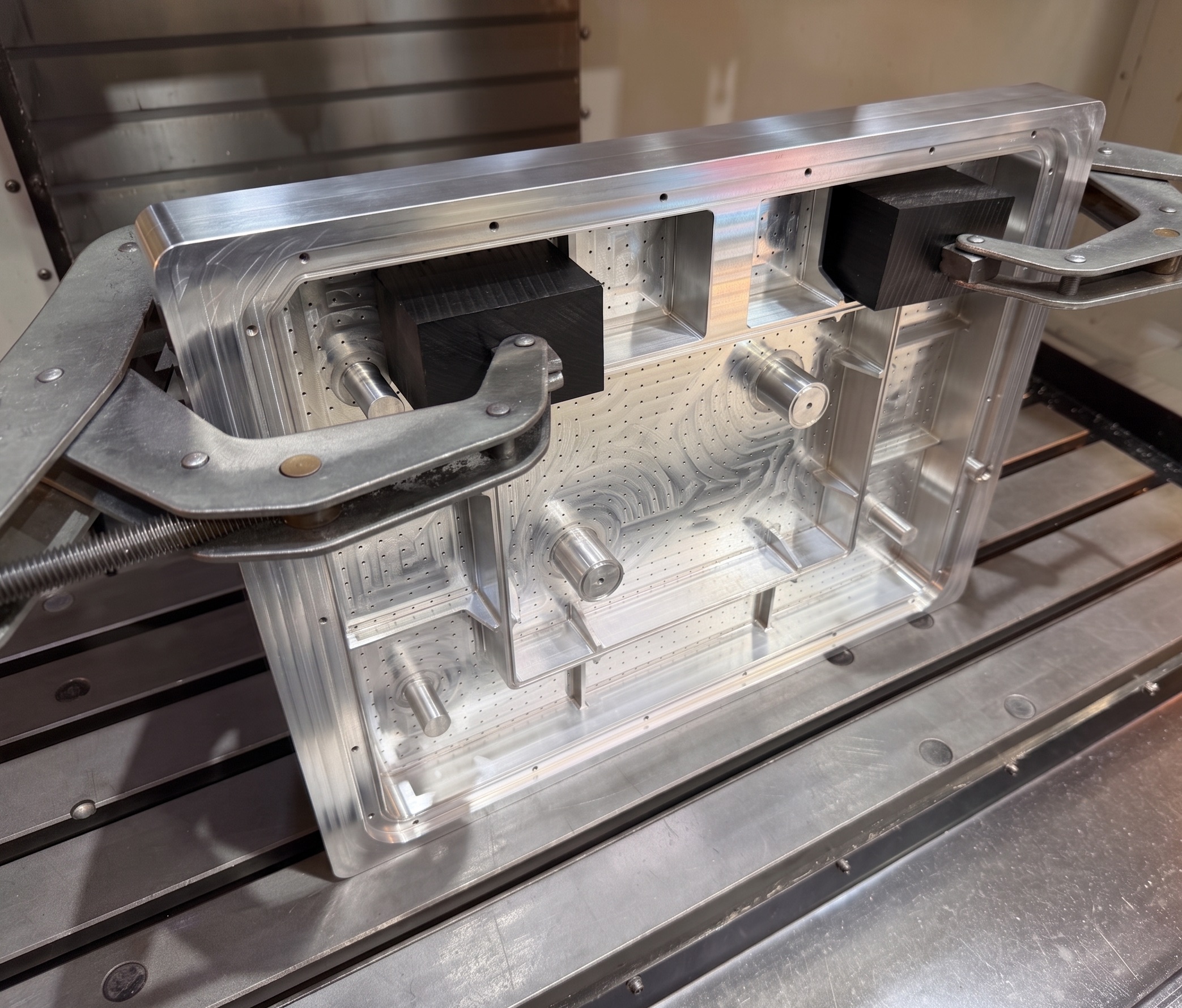 A large aluminium frame held with toe clamps and being machined on a CNC mill.