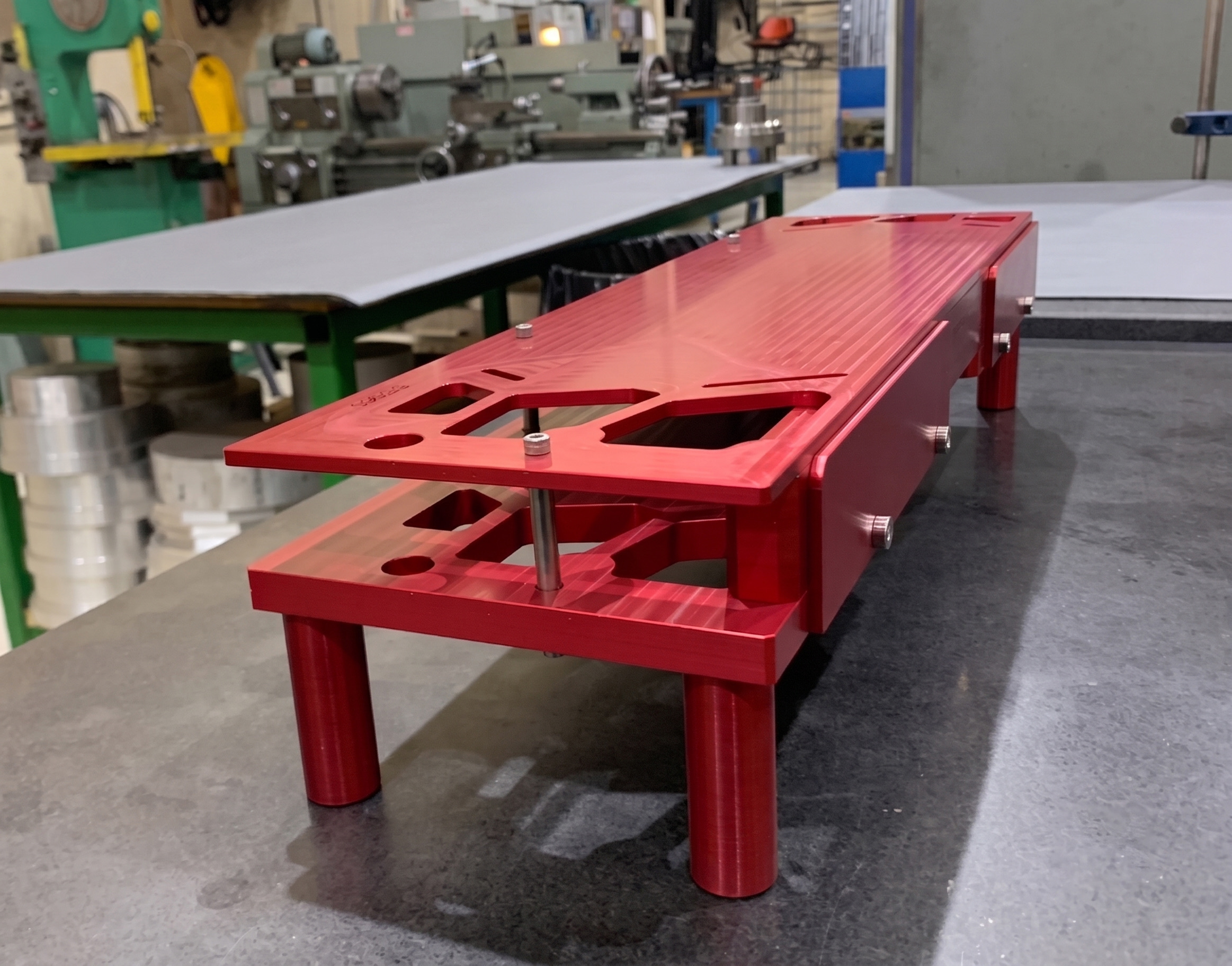 A red-anodised machined aluminium fixture assembly on the production floor.