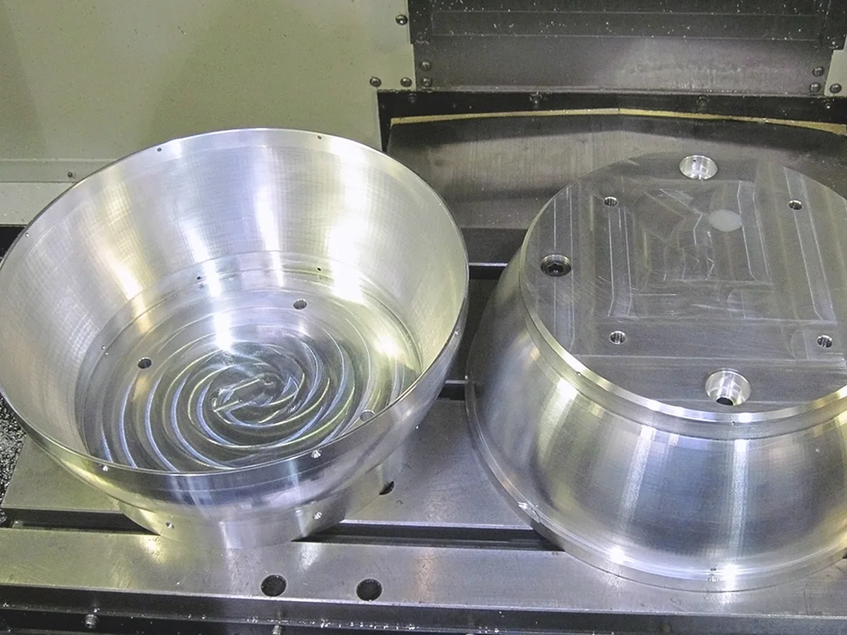 Two large machined aluminum domes on a machine table, one concave and one convex